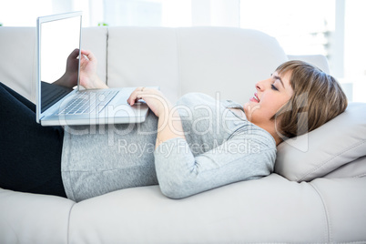 Smiling woman using laptop while lying on sofa