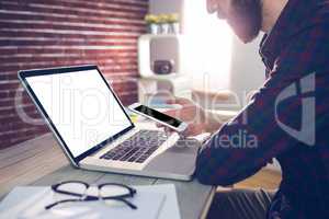 Midsection of graphic designer using smartphone and laptop