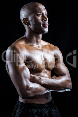 Shirtless athlete standing with arms crossed while looking away