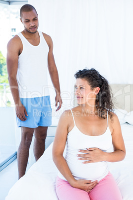 Husband looking at pregnant wife sitting on bed