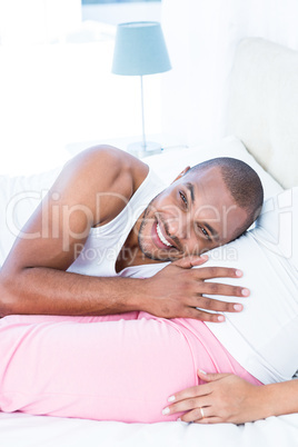 Happy man listening to belly of pregnant wife lying on bed