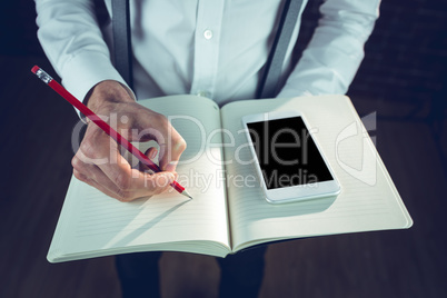 Midsection of businessman using smartphone while writing
