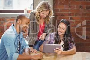 Smiling business people discussing over tablet in creative offic