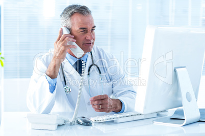 Male doctor holding telephone while looking at computer in hospi