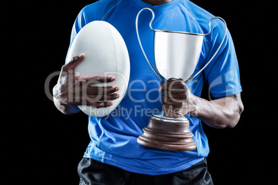 Mid section of sportsman holding trophy and rugby ball