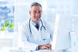 Smiling male doctor using computer in clinic