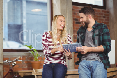 Creative colleagues smiling while discussing over tablet