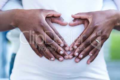 Mid section of couple forming heart shape on belly