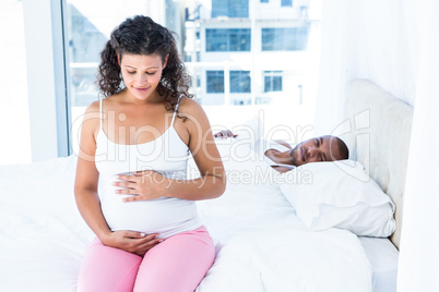 Husband lying on bed and looking at pregnant wife