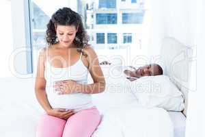 Husband lying on bed and looking at pregnant wife