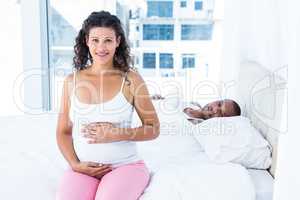 Pregnant wife sitting while husband lying on bed