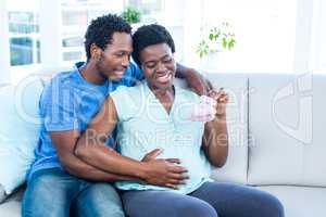 Happy pregnant woman holding baby shoes while sitting on sofa