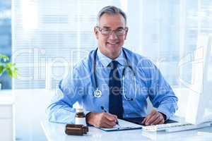 Portrait of smiling male doctor writing on document in clinic