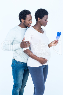 Pregnant wife holding color swatches while standing with husband