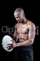 Concentrated shirtless athlete looking down while holding rugby