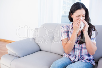 Pretty brunette sneezing on tissue on couch