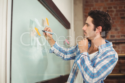 Businessman holding marker while standing by glass board