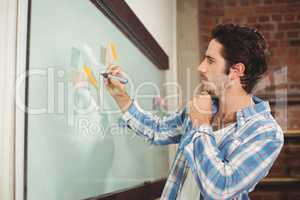 Businessman holding marker while standing by glass board