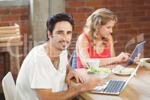 Portrait of businessman using laptop with colleague in backgroun