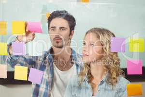 Woman looking at man sticking notes on glass