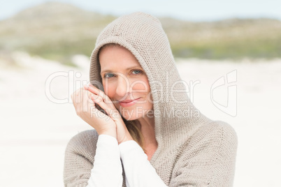 Smiling woman standing on the sand with hood up