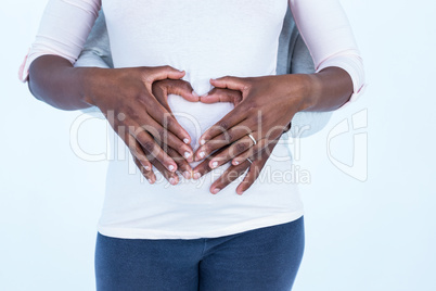 Husband making heart shape on belly of pregnant wife