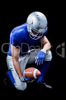 American football player kneeling while holding ball