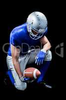 American football player kneeling while holding ball