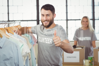 Portrait of happy man gesturing thumbs up while selecting clothe