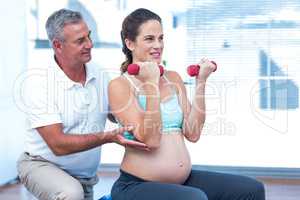 Instructor assisting pregnant woman in lifting dumbbells