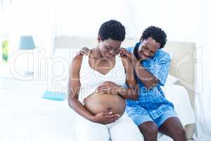 Man massaging pregnant wife while sitting on bed