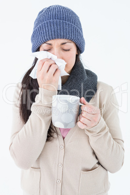 Sick brunette blowing her nose while holding a mug