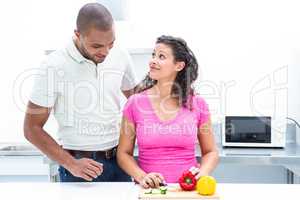 Pregnant wife looking at husband while chopping vegetable