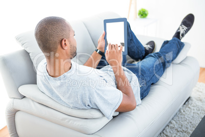 Young man reclining on sofa using tablet