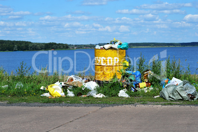 Overflowing barrel with rubbish and waste disposal on the waterf