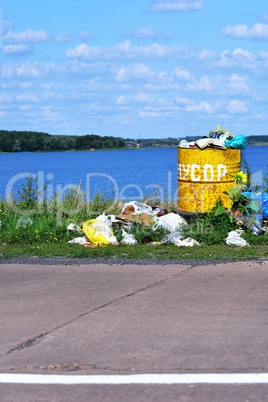 Overflowing barrel with rubbish and waste disposal on the waterf