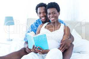 Portrait of pregnant woman and her husband reading book
