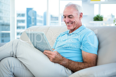 Senior man sitting on sofa while using digital tablet