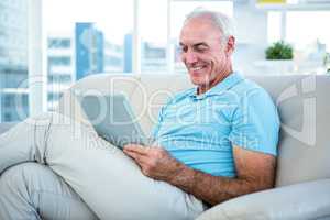 Senior man sitting on sofa while using digital tablet