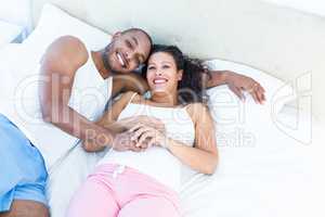 Portrait of happy pregnant wife with husband lying on bed