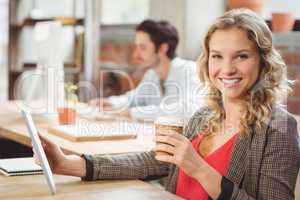 Portrait of smiling woman holding coffee and digital tablet