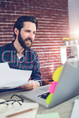 Smiling creative businessman with documents using laptop