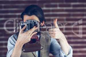 Hipster showing thumbs up gesture while photographing