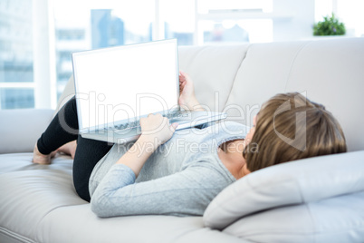 Woman using laptop while lying on sofa