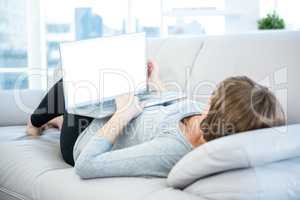 Woman using laptop while lying on sofa