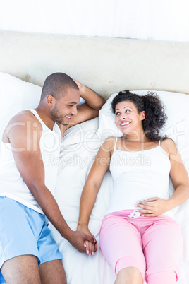 Cheerful pregnant woman lying on bed with husband