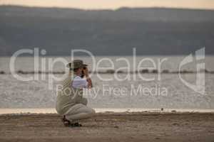 Kneeling man in hat takes lakeside picture