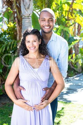 Portrait of happy husband with pregnant wife touching belly