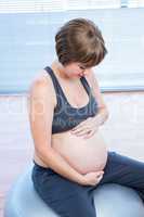 Pregnant woman holding belly while sitting on fitness ball