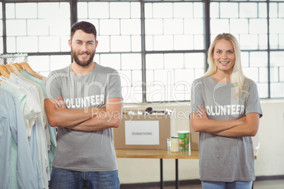 Portrait of volunteers with arms crossed standing by clothes rac